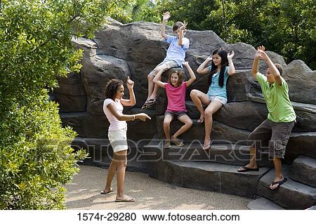 Teenagers with their arms raised sitting on rocks and playing View Large Photo Image Stock Image - Teenagers with their arms raised sitting on rocks and playing. Fotosearch