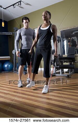 Stock Image - Trainer instructing a young woman in the gym. Fotosearch