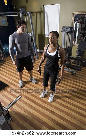 Stock Image - Trainer instructing a young woman in the gym. Fotosearch