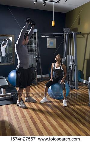 Stock Photo - Trainer instructing a young woman in the gym. Fotosearch