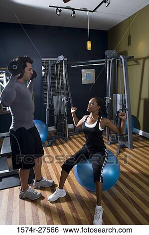 Stock Photograph - Trainer instructing a young woman in the gym. Fotosearch