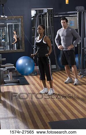 Trainer instructing a young woman in the gym View Large Photo Image Stock Photography - Trainer instructing a young woman in the gym. Fotosearch