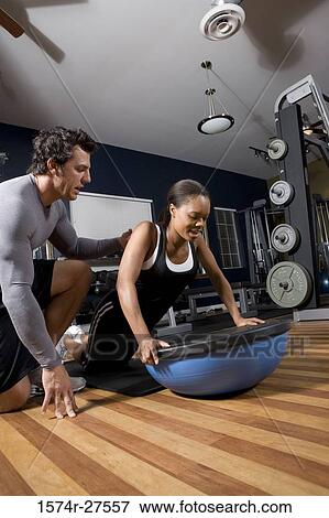 Stock Photo - Trainer instructing a young woman on a fitness ball in the gym. Fotosearch