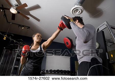 Trainer instructing a young woman with boxing equipment in the gym View Large Photo Image Stock Image - Trainer instructing a young woman with boxing equipment in the gym. Fotosearch