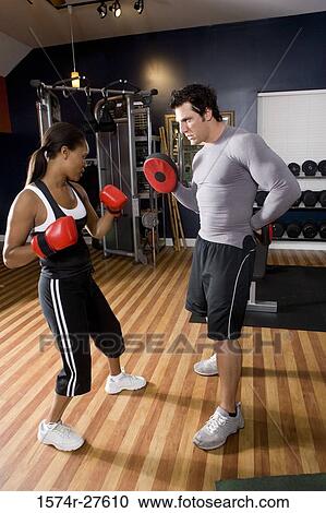 Trainer instructing a young woman with boxing equipment in the gym View Large Photo Image Stock Image - Trainer instructing a young woman with boxing equipment in the gym. Fotosearch