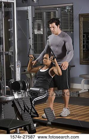 Trainer instructing a young woman with sports equipment in the gym View Large Photo Image Stock Photo - Trainer instructing a young woman with sports equipment in the gym. Fotosearch