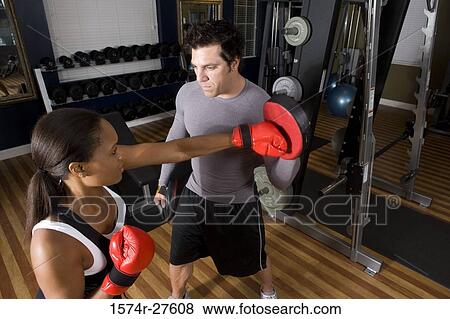Trainer instructing a young woman with boxing equipment in the gym View Large Photo Image Stock Photo - Trainer instructing a young woman with boxing equipment in the gym. Fotosearch
