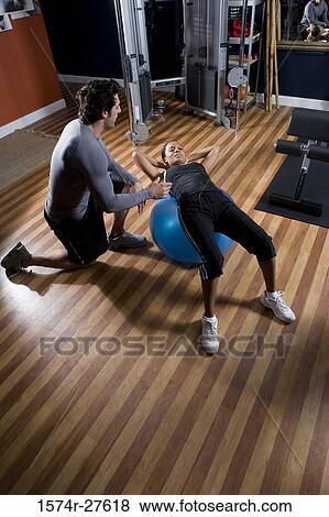 Trainer instructing a young woman with fitness ball in the gym View Large Photo Image Stock Photo - Trainer instructing a young woman with fitness ball in the gym. Fotosearch