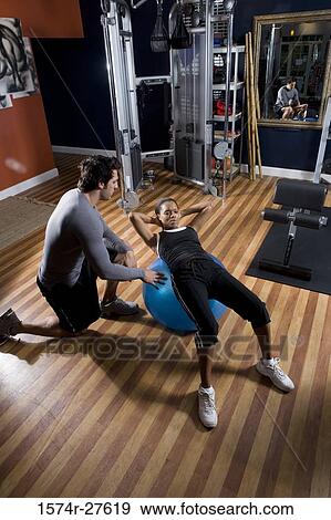 Trainer instructing a young woman with fitness ball in the gym View Large Photo Image Stock Photo - Trainer instructing a young woman with fitness ball in the gym. Fotosearch