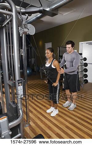 Trainer instructing a young woman with sports equipment in the gym View Large Photo Image Stock Photograph - Trainer instructing a young woman with sports equipment in the gym. Fotosearch
