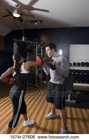 Stock Photograph - Trainer instructing a young woman with boxing equipment in the gym. Fotosearch