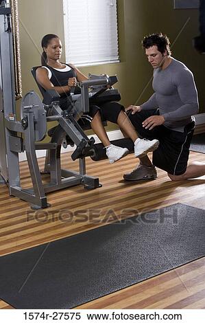 Stock Photography - Trainer instructing a young woman with sports equipment in the gym. Fotosearch