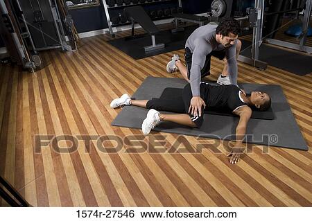 Stock Photograph - Trainer stretching leg of a young woman in the gym. Fotosearch
