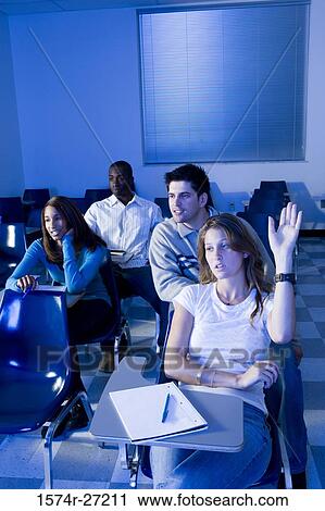 Stock Image - University students attending lecture while one student with hand raised in the classroom. Fotosearch