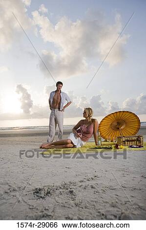 View of a young couple conversing at the beach View Large Photo Image Stock Photograph - View of a young couple conversing at the beach. Fotosearch