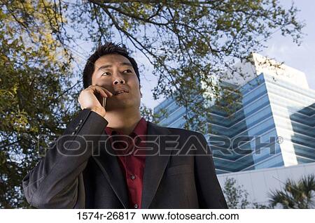 Young businessman using mobile phone in front of a building exterior View Large Photo Image Stock Photo - Young businessman using mobile phone in front of a building exterior. Fotosearch
