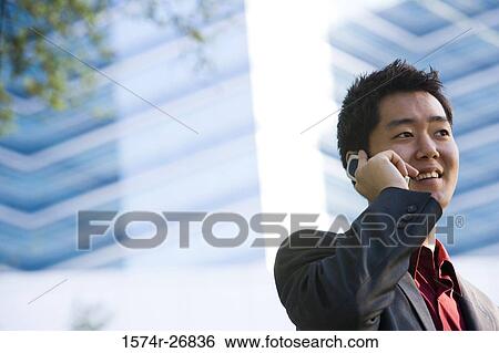 Stock Photograph - Young businessman using mobile phone in front of a building exterior. Fotosearch