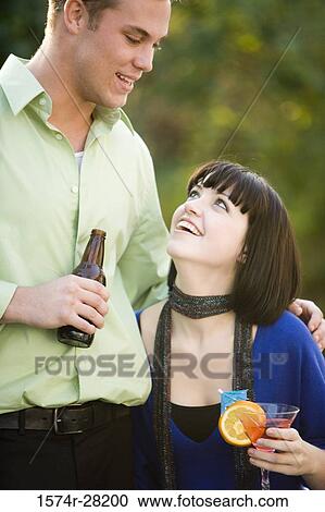 Young couple holding drinks and looking at each other View Large Photo Image Stock Image - Young couple holding drinks and looking at each other. Fotosearch