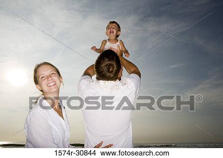 Picture - Young couple playing with daughter on the beach. Fotosearch
