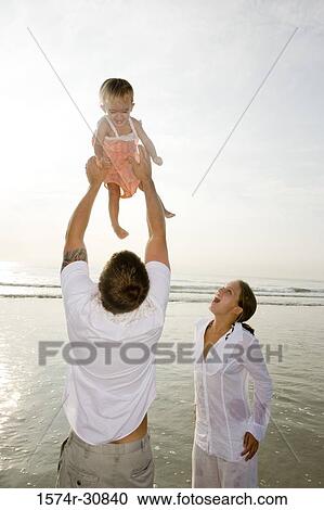 Stock Image - Young couple playing with daughter on the beach. Fotosearch
