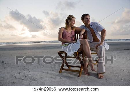 Stock Photograph - Young couple relaxing on chairs at the beach. Fotosearch