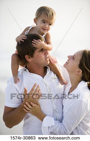 Young couple with girl sitting on father's shoulder at beach View Large Photo Image Stock Image - Young couple with girl sitting on father's shoulder at beach. Fotosearch