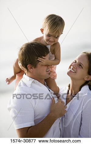 Stock Photo - Young couple with girl sitting on father's shoulder at beach. Fotosearch