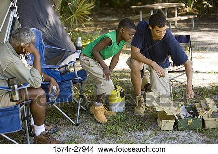 Young man and a boy looking in a fishing tackle box while mature man sitting on a chair by tent View Large Photo Image Picture - Young man and a boy looking in a fishing tackle box while mature man sitting on a chair by tent. Fotosearch