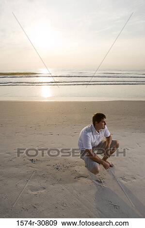 Young man crouching on the beach View Large Photo Image Stock Photo - Young man crouching on the beach. Fotosearch