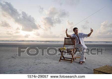 Young man gesturing while sitting on a chair at the beach View Large Photo Image Stock Photo - Young man gesturing while sitting on a chair at the beach. Fotosearch