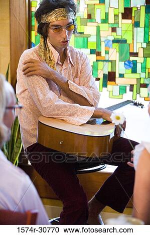 Stock Image - Young man holding a guitar and in conversation with women. Fotosearch