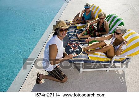 Young man holding tray of drinks in front of senior women lying on reclining chairs View Large Photo Image Picture - Young man holding tray of drinks in front of senior women lying on reclining chairs. Fotosearch