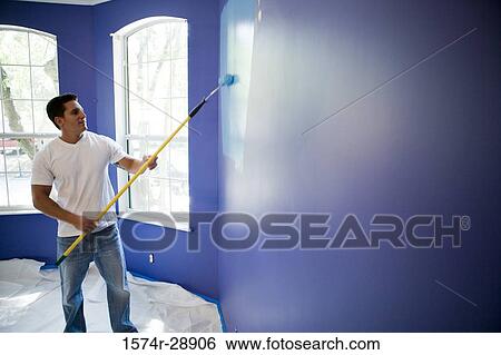 Stock Photograph - Young man painting wall with paint roller in house. Fotosearch