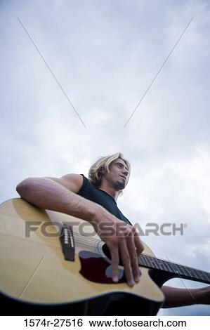 Young man playing a guitar against sky View Large Photo Image Stock Photograph - Young man playing a guitar against sky. Fotosearch