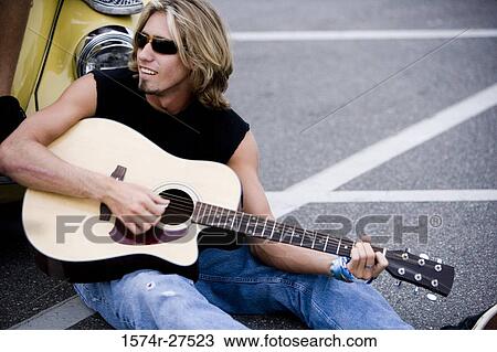 Stock Image - Young man playing a guitar by a car at the parking area. Fotosearch