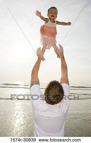 Stock Photo - Young man playing with his daughter on the beach. Fotosearch