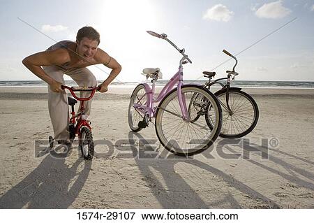Young man riding a kid's cycle at the beach View Large Photo Image Stock Photo - Young man riding a kid's cycle at the beach. Fotosearch