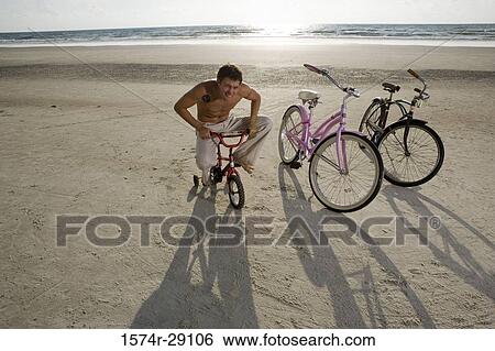 Young man riding a kid's cycle at the beach View Large Photo Image Stock Photograph - Young man riding a kid's cycle at the beach. Fotosearch