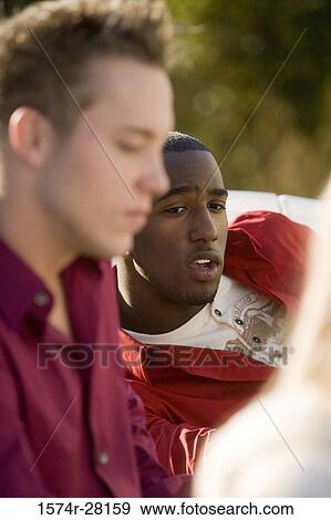Stock Photo - Young man sitting on armchair by other. Fotosearch