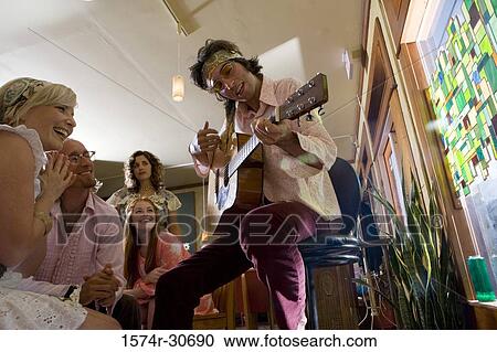 Stock Image - Young man sitting with a guitar while others beside. Fotosearch