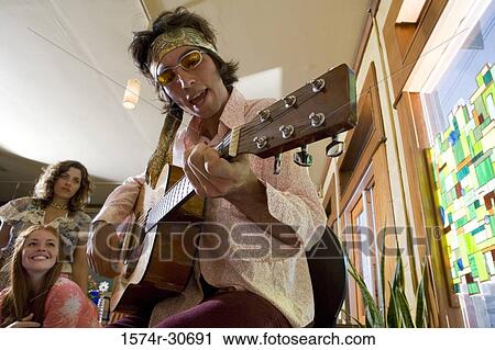 Stock Image - Young man sitting with a guitar while others beside. Fotosearch