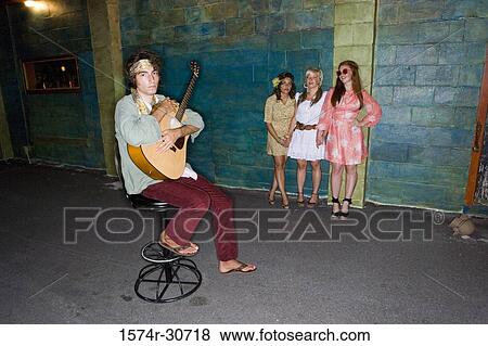 Stock Photo - Young man sitting with guitar while woman standing by wall. Fotosearch