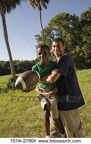 Picture - Young man with a boy holding football at forest. Fotosearch