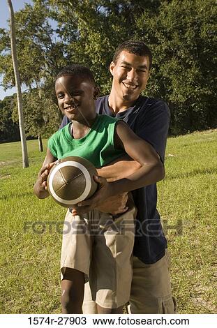 Young man with a boy holding football at forest View Large Photo Image Stock Image - Young man with a boy holding football at forest. Fotosearch