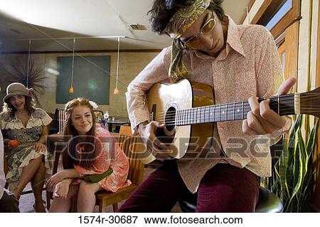 Young man with a guitar while sisters sitting behind View Large Photo Image Stock Photo - Young man with a guitar while sisters sitting behind. Fotosearch