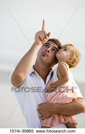 Stock Photography - Young man with his daughter on the beach looking up. Fotosearch