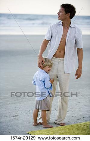 Young man with son standing at the beach View Large Photo Image Stock Photo - Young man with son standing at the beach. Fotosearch
