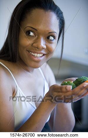 Stock Image - Young woman holding vegetables on her palm in the kitchen. Fotosearch