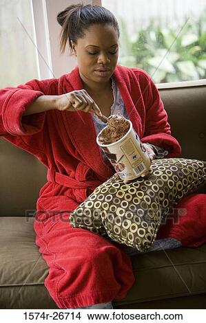 Young woman in gown holding an ice cream cup on a sofa View Large Photo Image Picture - Young woman in gown holding an ice cream cup on a sofa. Fotosearch