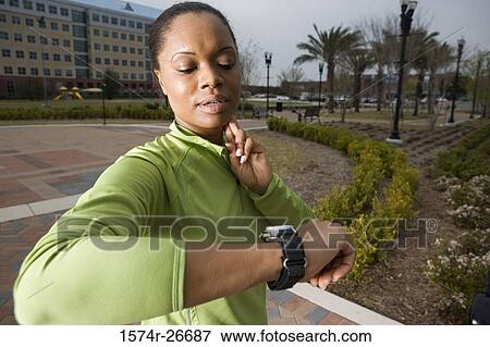 Young woman in sports clothing looking her watch with building in the background View Large Photo Image Stock Photo - Young woman in sports clothing looking her watch with building in the background. Fotosearch